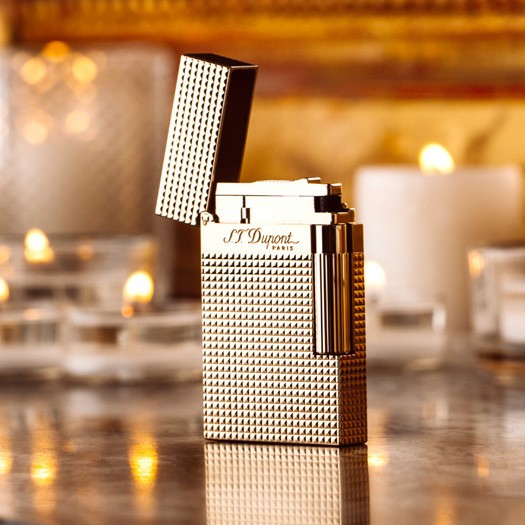 S.T. Dupont Ligne 2 Yellow Gold (16284 / REF. 016284) е емблематична луксозна запалка, съчетаваща масивен месингов корпус, финиш в жълто злато и прецизна Diamond Head декорация. Множеството геометрични фасети улавят и пречупват светлината, придавайки на златистата повърхност характерен динамичен блясък. Моделът е оборудван с двоен мек пламък и носи характерното акустично усещане при отваряне, с което Ligne 2 е известна сред ценителите. С класически размери 37 × 62 × 11 mm, 16284 съчетава солидно присъствие, прецизна механика и неподвластна на времето елегантност – истинска златна класика в света на S.T. Dupont.
